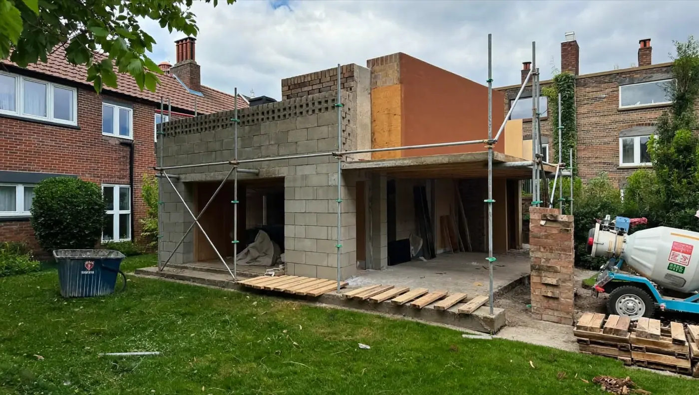 Rear extension under construction: blockwork walls, scaffolding, a mixer and a skip on the lawn