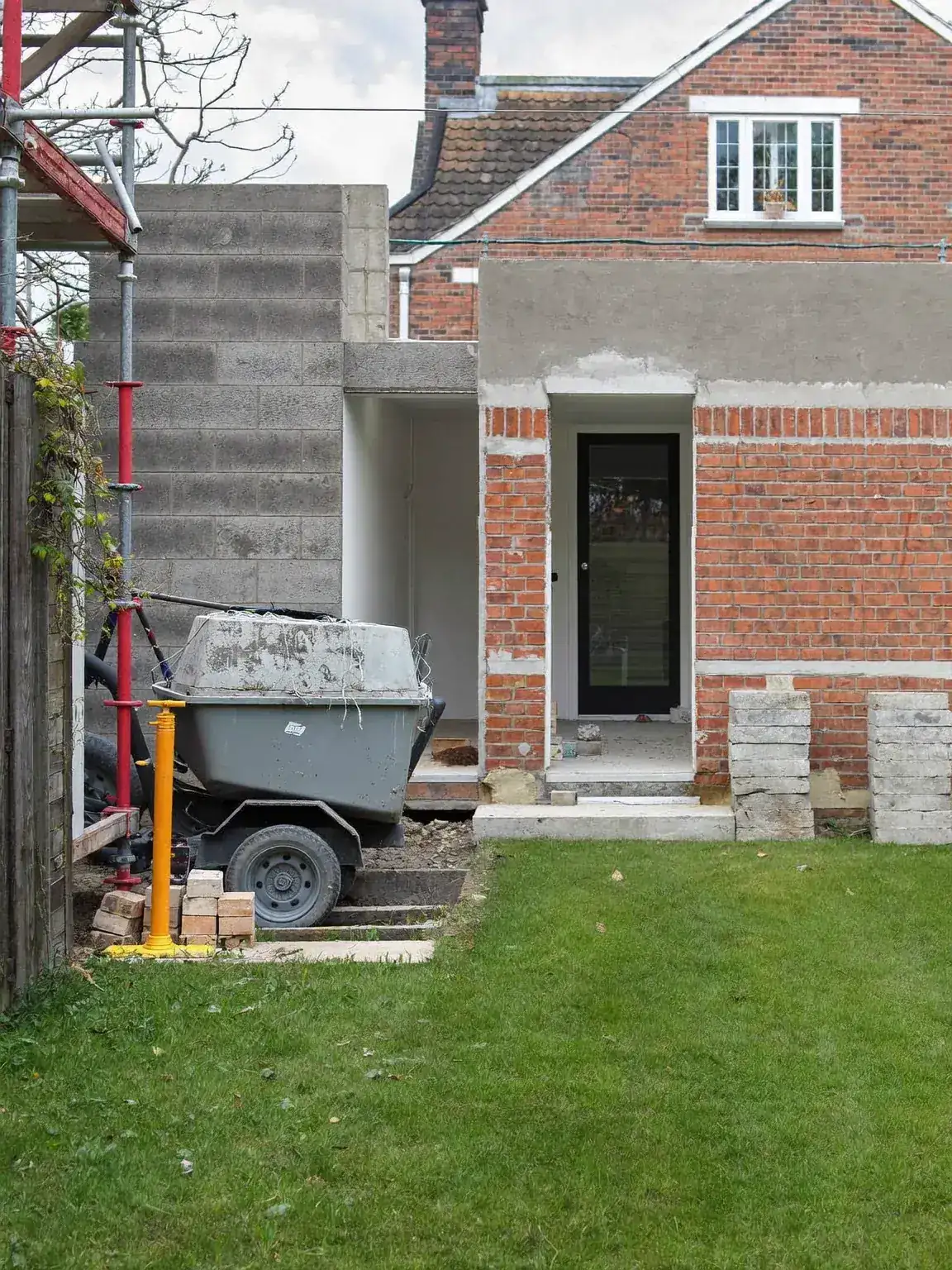 Brick and blockwork walls rising on a rear extension, with a concrete mixer and steel props in the foreground
