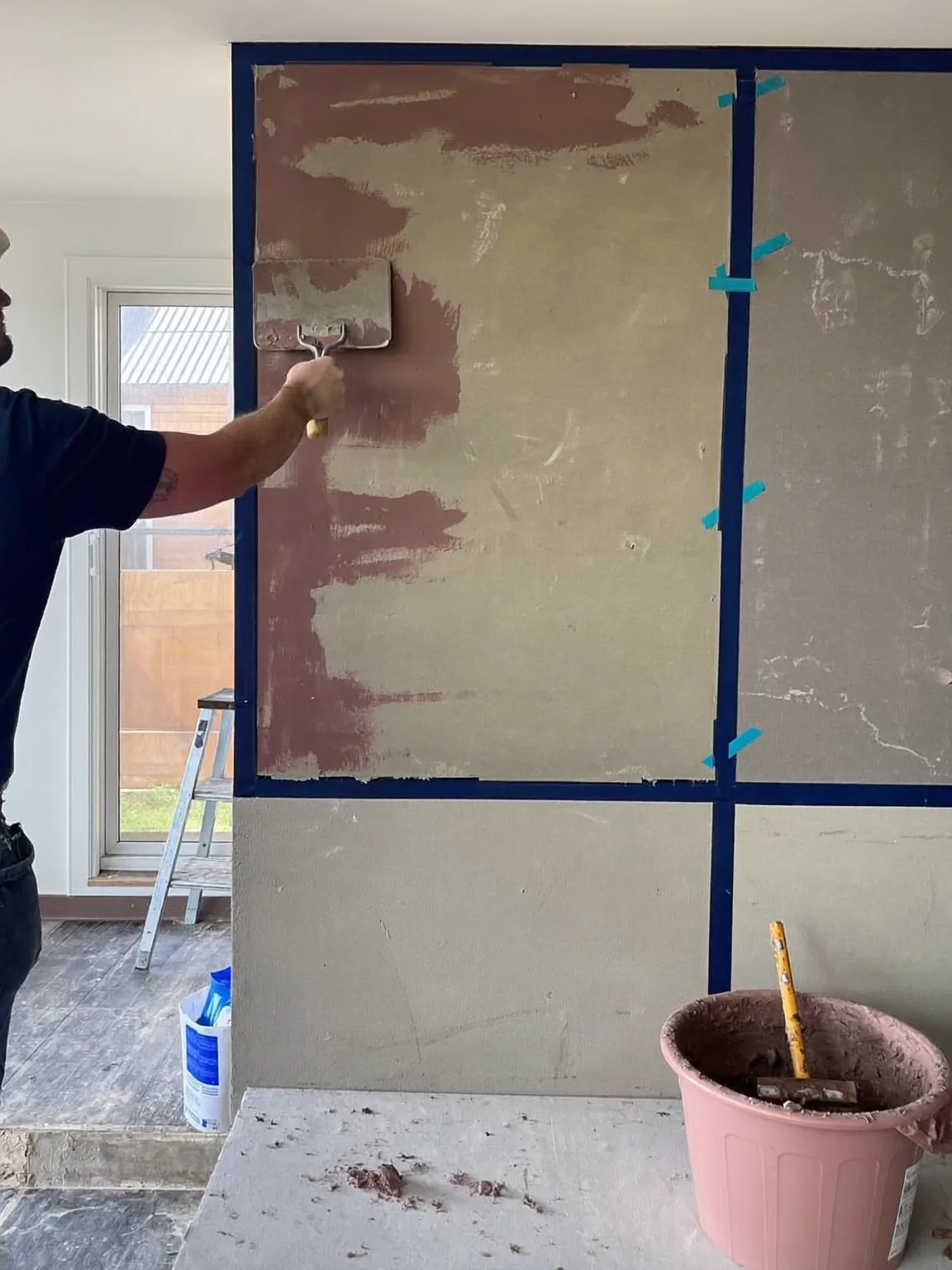 A worker rolling primer onto a plasterboard wall with taped joints in an unfinished room