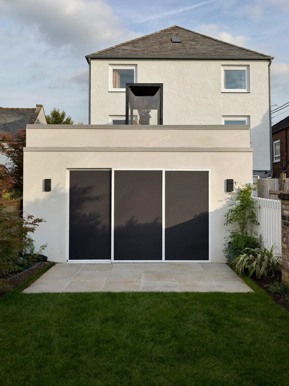 Cream-rendered rear extension with dark sliding glass doors and a sandstone patio