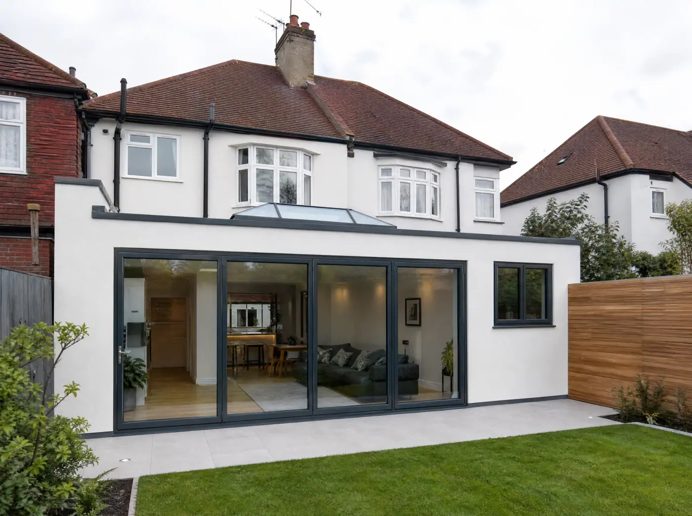 White-rendered single-storey rear extension with black-framed sliding doors, a roof lantern and a lawn