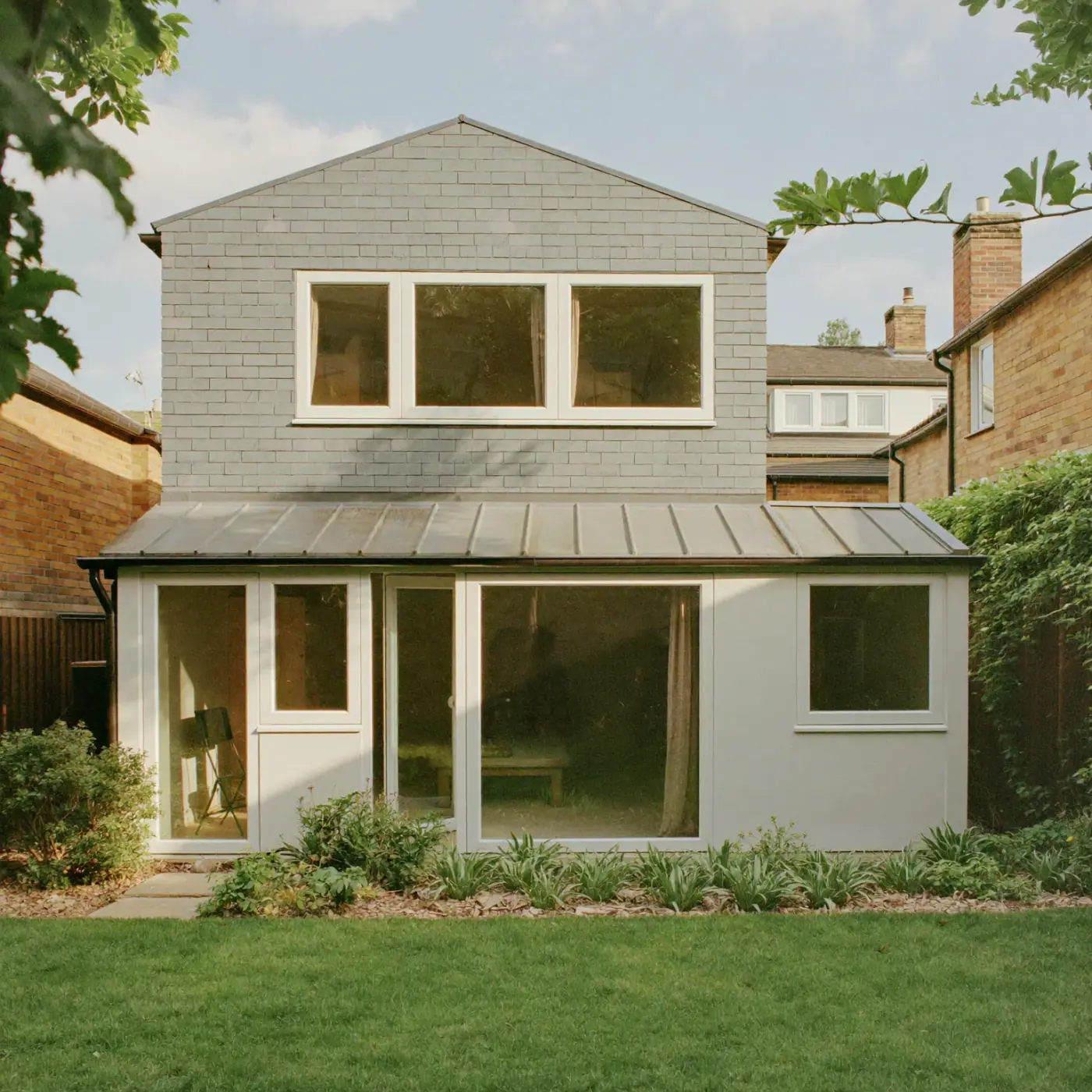 Rear of a house with a loft dormer above a single-storey extension, a zinc roof and glazed doors