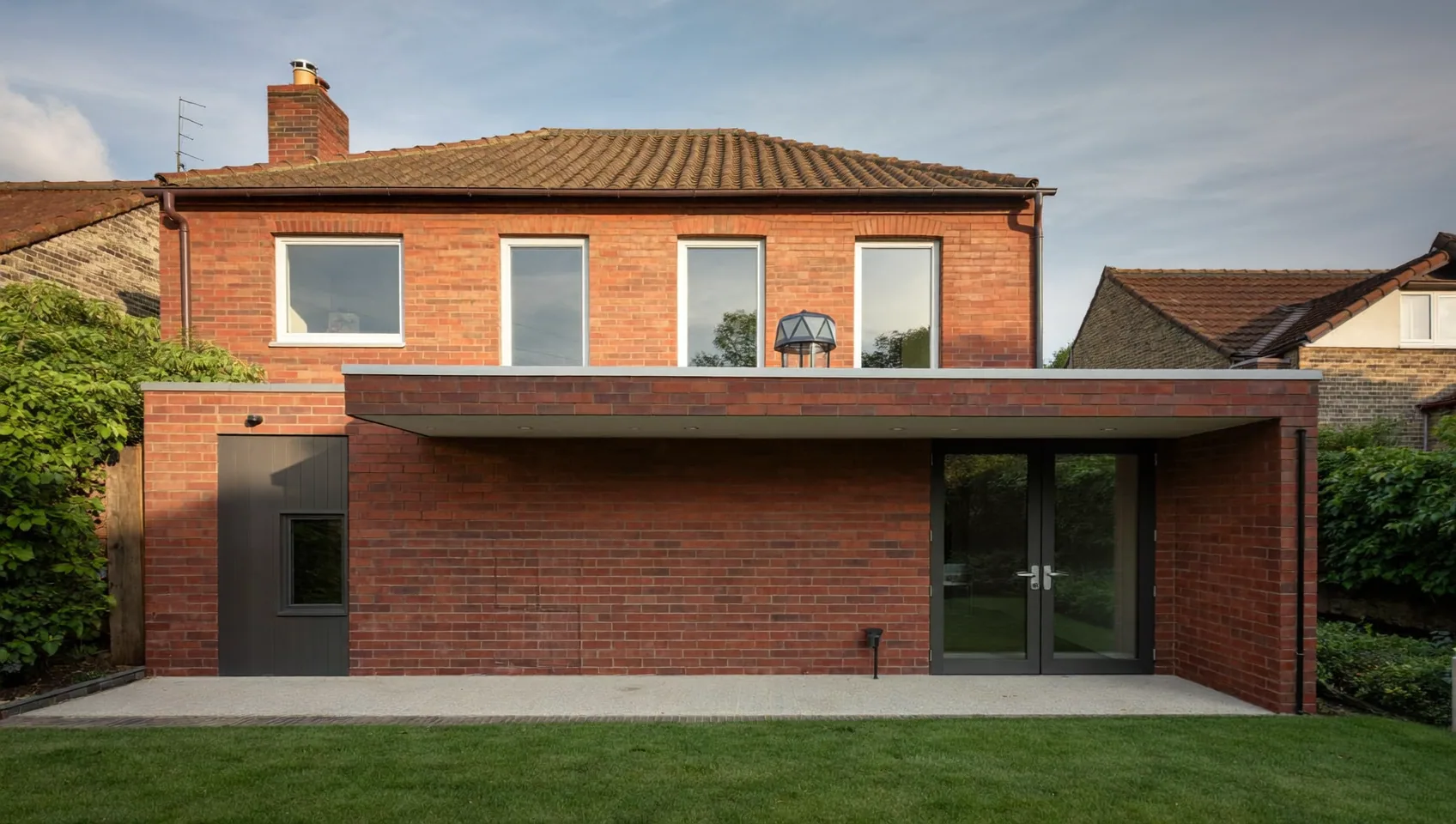 Single-storey brick rear extension with a flat roof, double doors and a tiled house behind