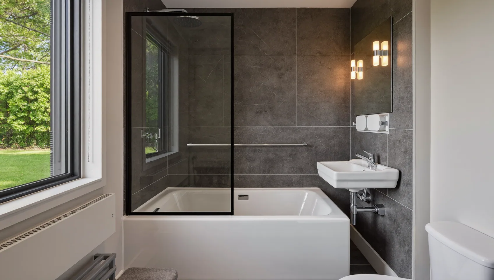 Modern bathroom with dark tiles, a bath with a glass screen and a wall-hung basin