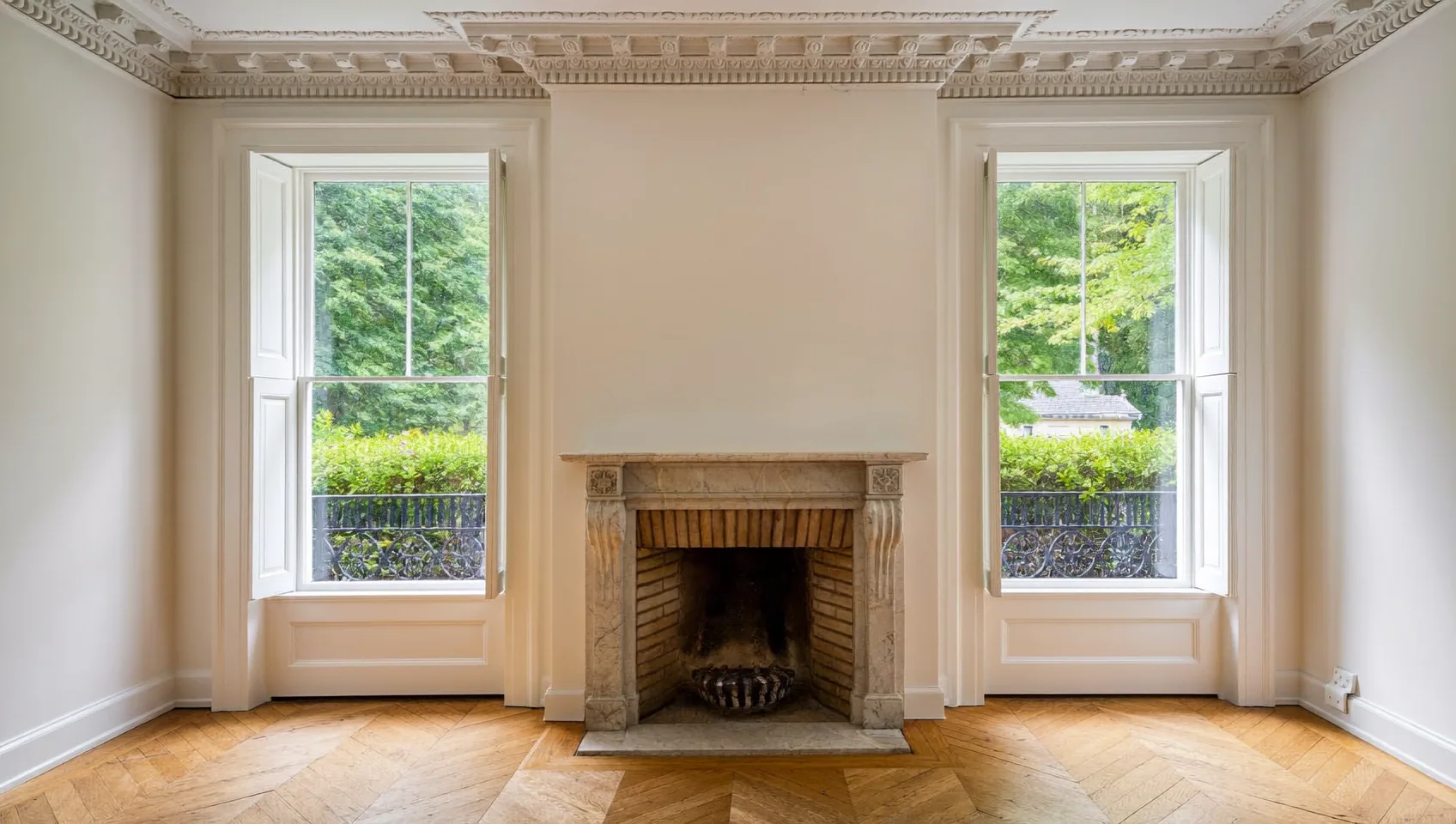 Period reception room with ornate cornicing, a stone fireplace, sash windows and herringbone parquet