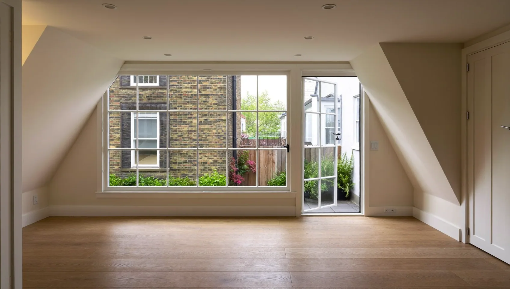 Converted basement or lower-ground room with oak flooring, a large window and French doors to a lightwell