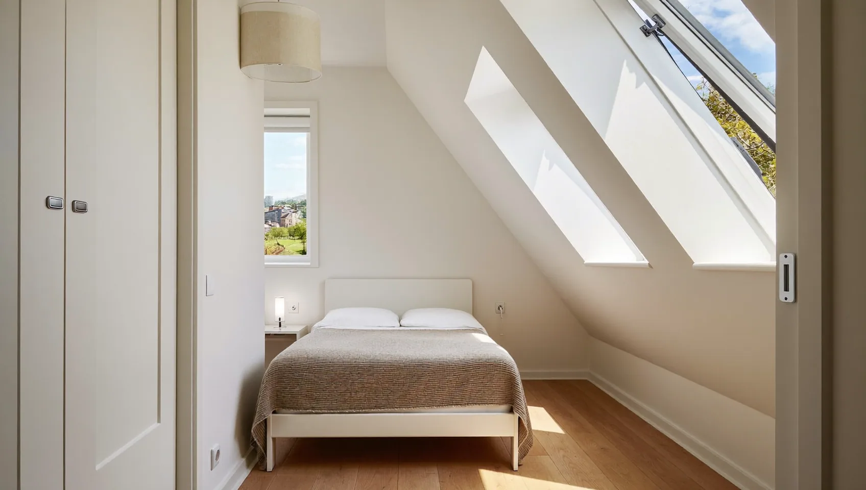 Loft bedroom with angled roof windows, a double bed and oak flooring