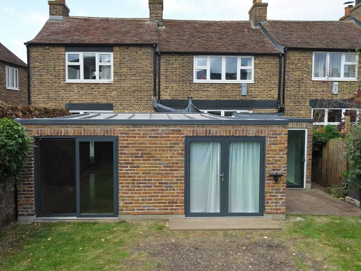 Amersham: L-shaped brick extension wrapping around the back and side of a house with dark sliding doors
