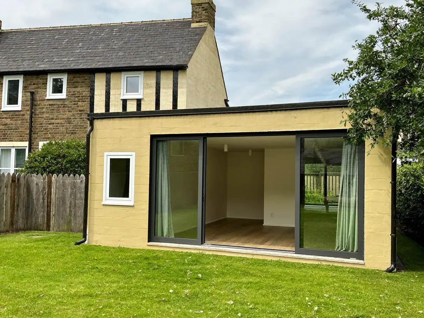 Cream-rendered flat-roofed rear extension with sliding glass doors beside a mock-Tudor house