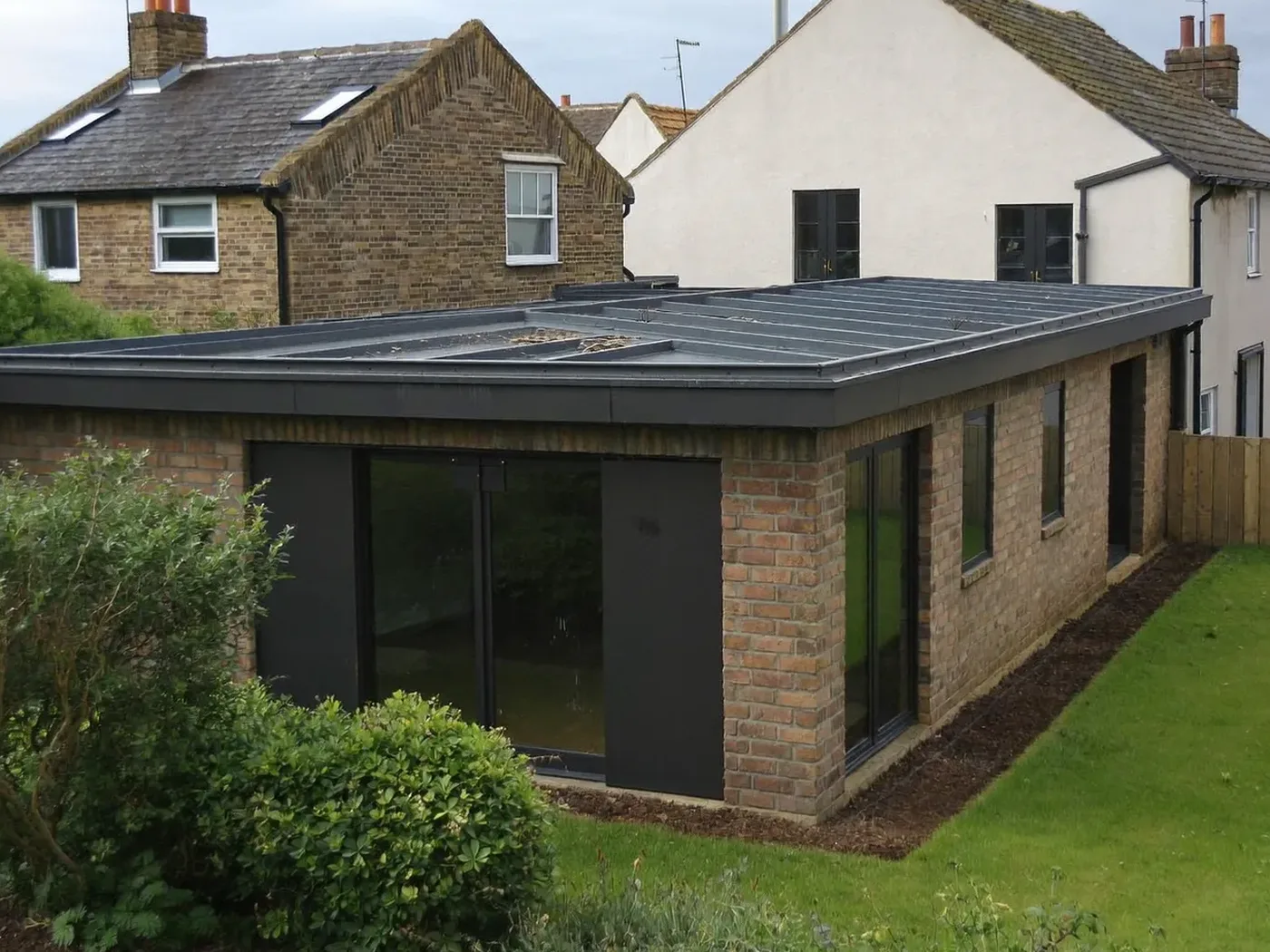 Beaconsfield: L-shaped brick extension wrapping around the back and side of a house with dark sliding doors