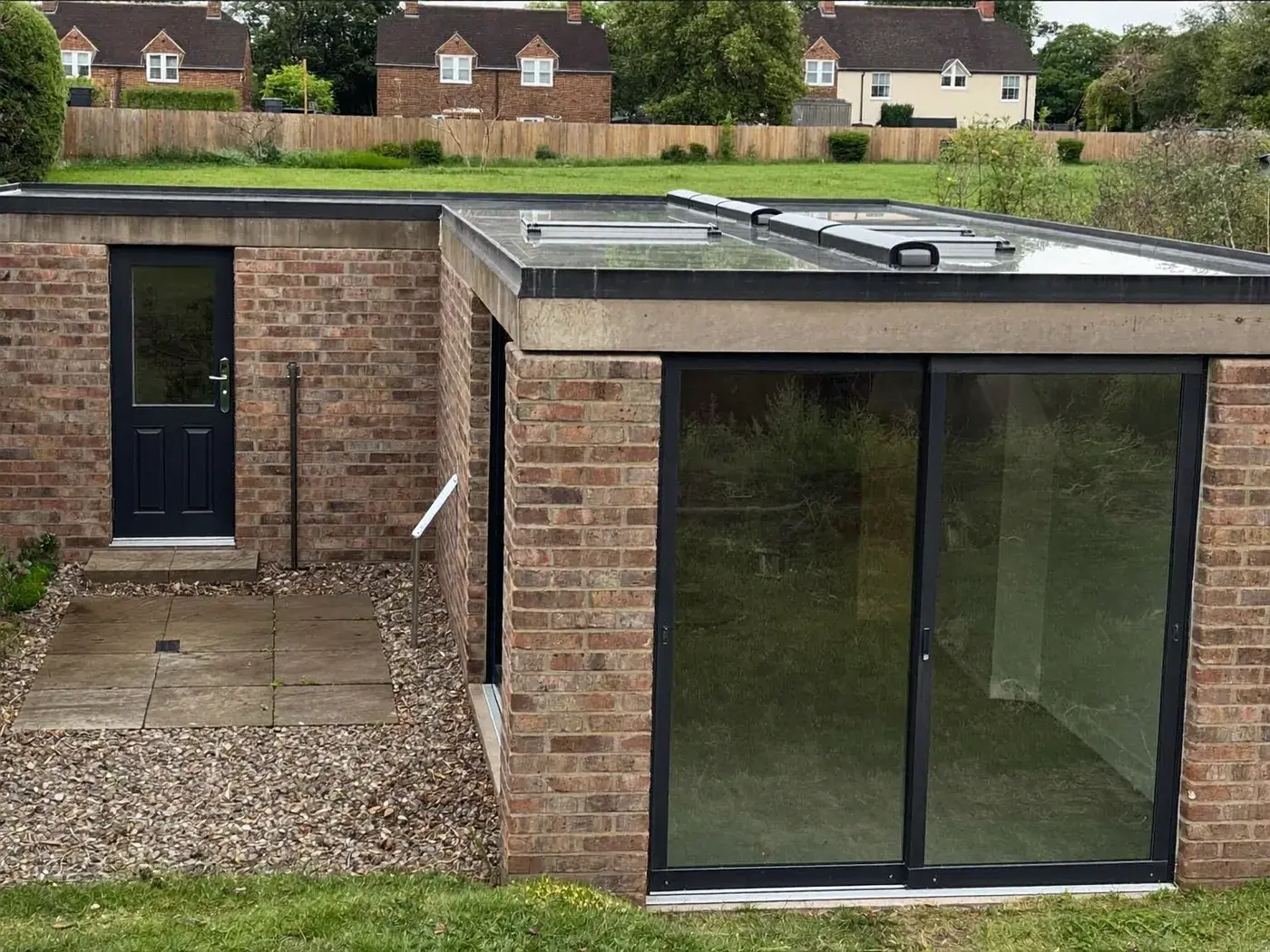 Borehamwood: L-shaped brick extension wrapping around the back and side of a house with dark sliding doors