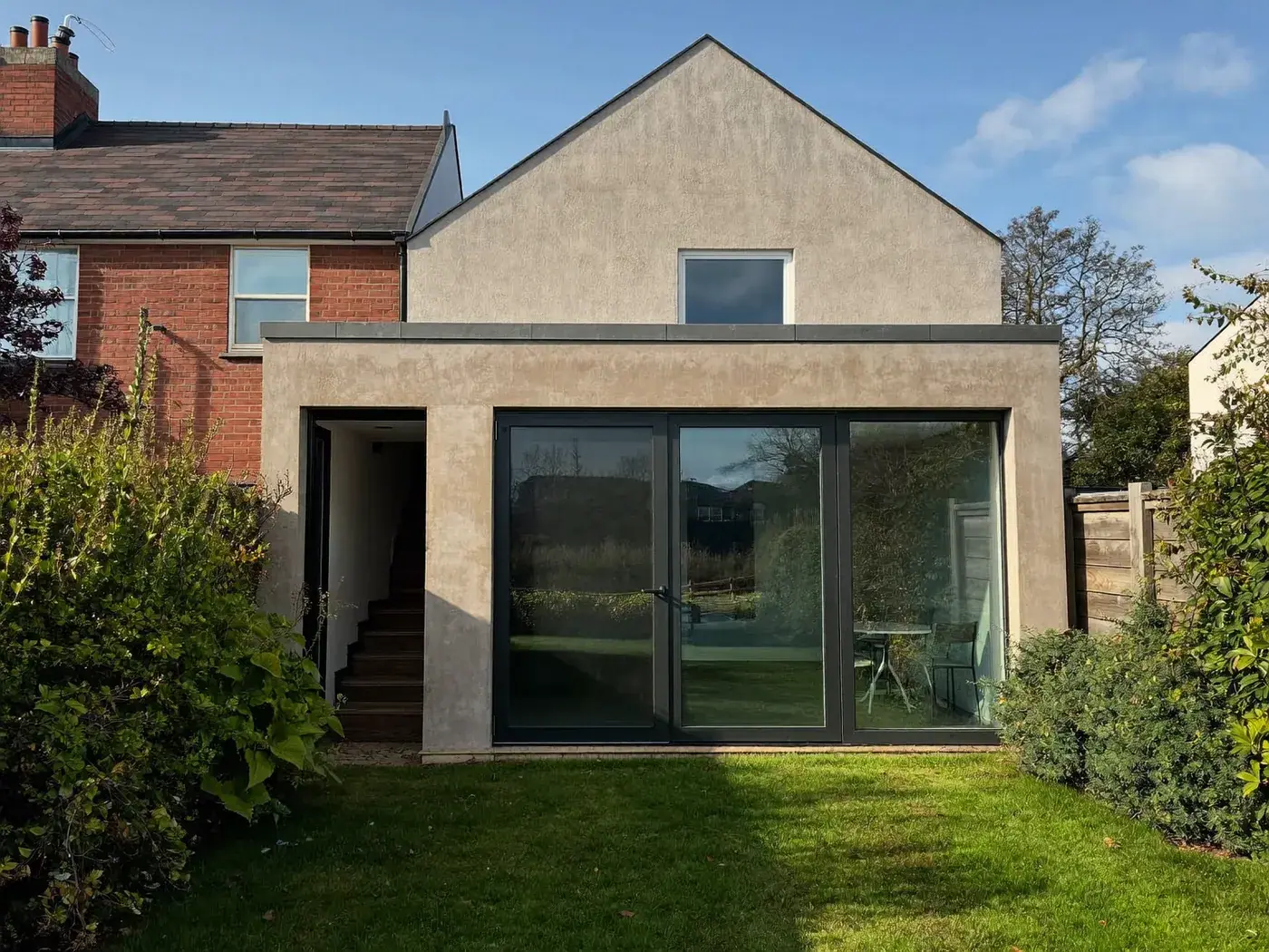 Bushey: single-storey brick rear extension with dark sliding doors onto a lawn