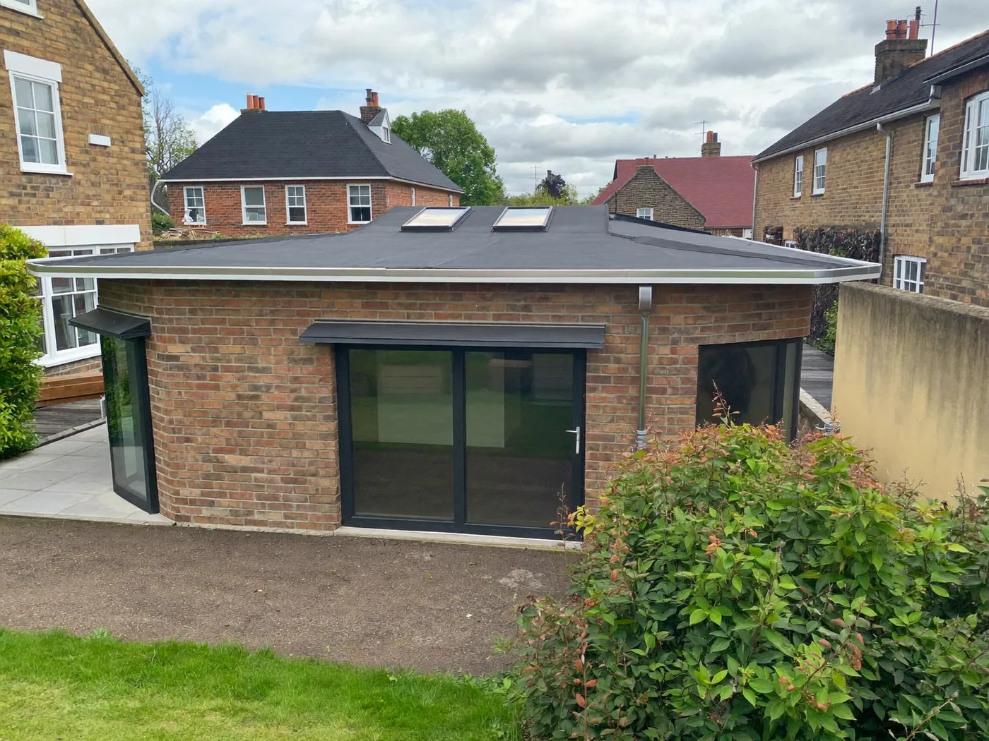 Bushey: L-shaped brick extension wrapping around the back and side of a house with dark sliding doors