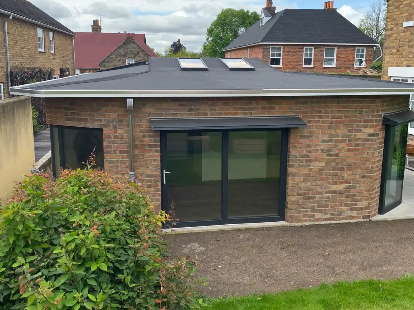 Croydon: L-shaped brick extension wrapping around the back and side of a house with dark sliding doors