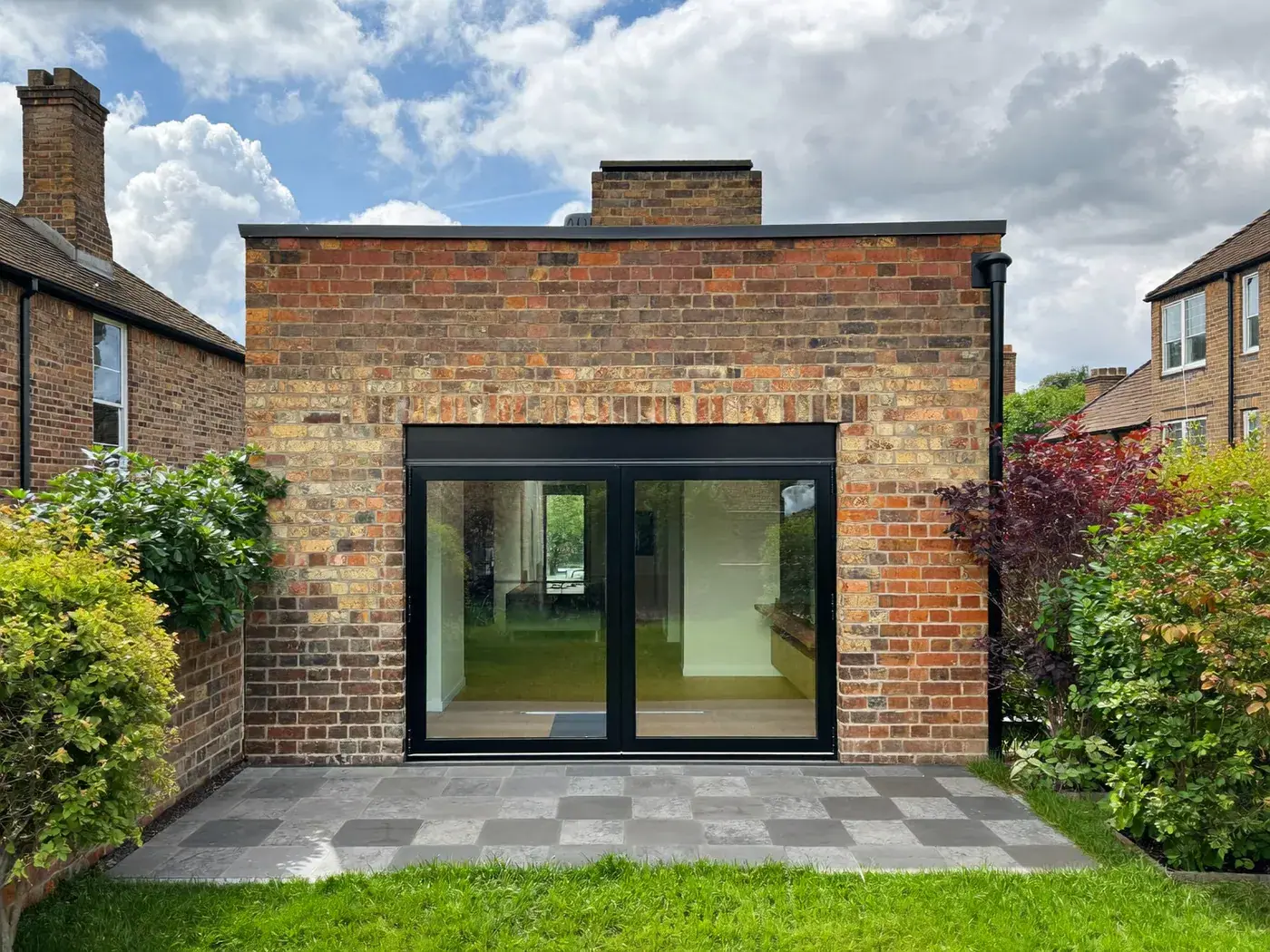 Ealing: single-storey brick rear extension with dark sliding doors onto a lawn