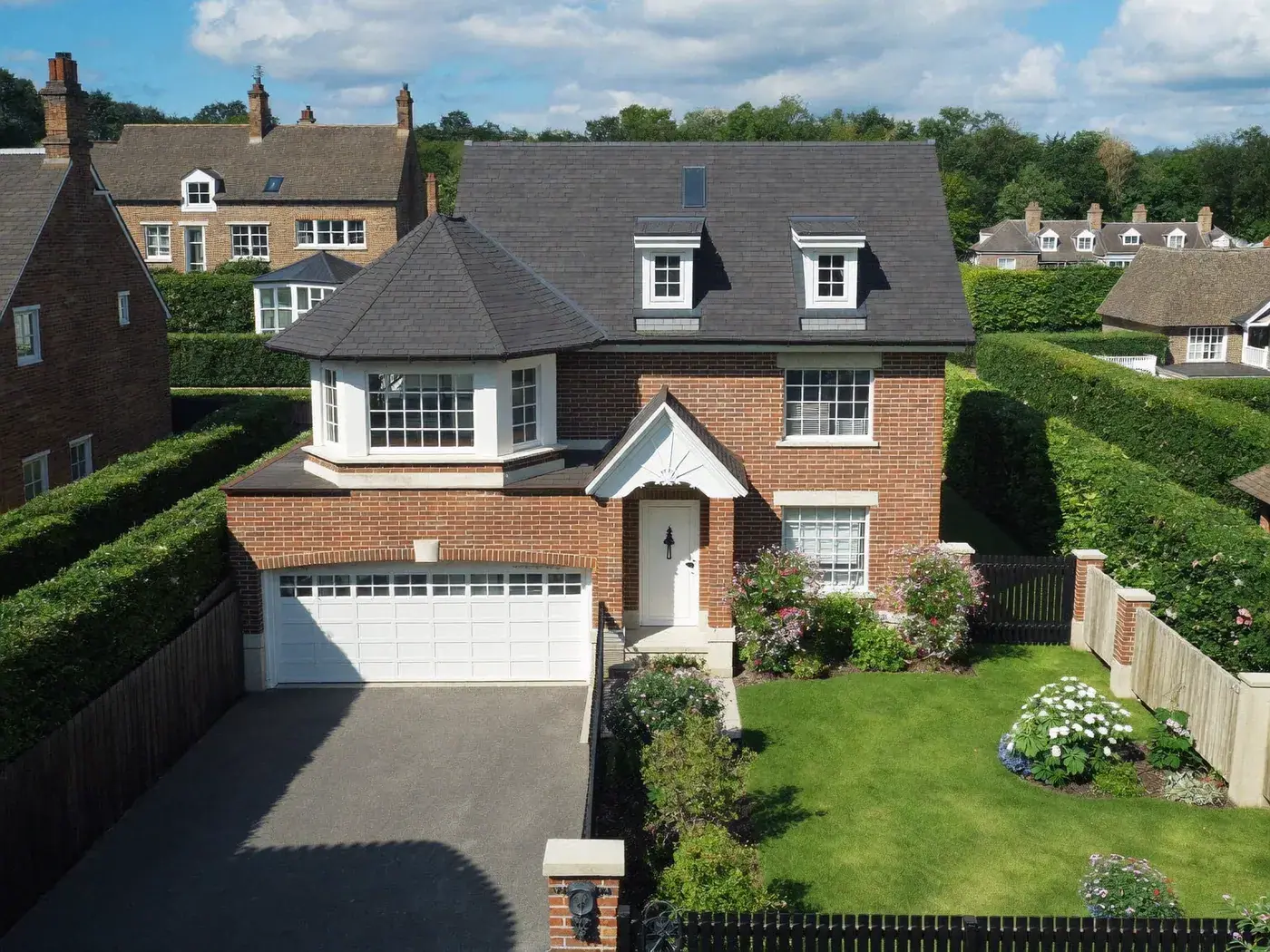 Detached red-brick house with a slate roof, dormer windows and a double garage, with a clipped hedge