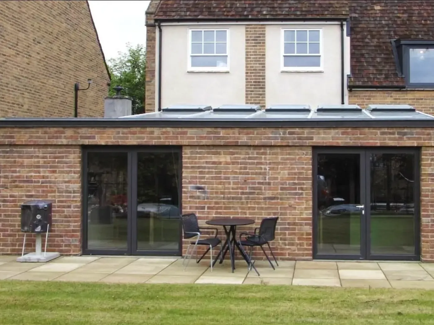 Egham: single-storey brick rear extension with dark sliding doors onto a lawn