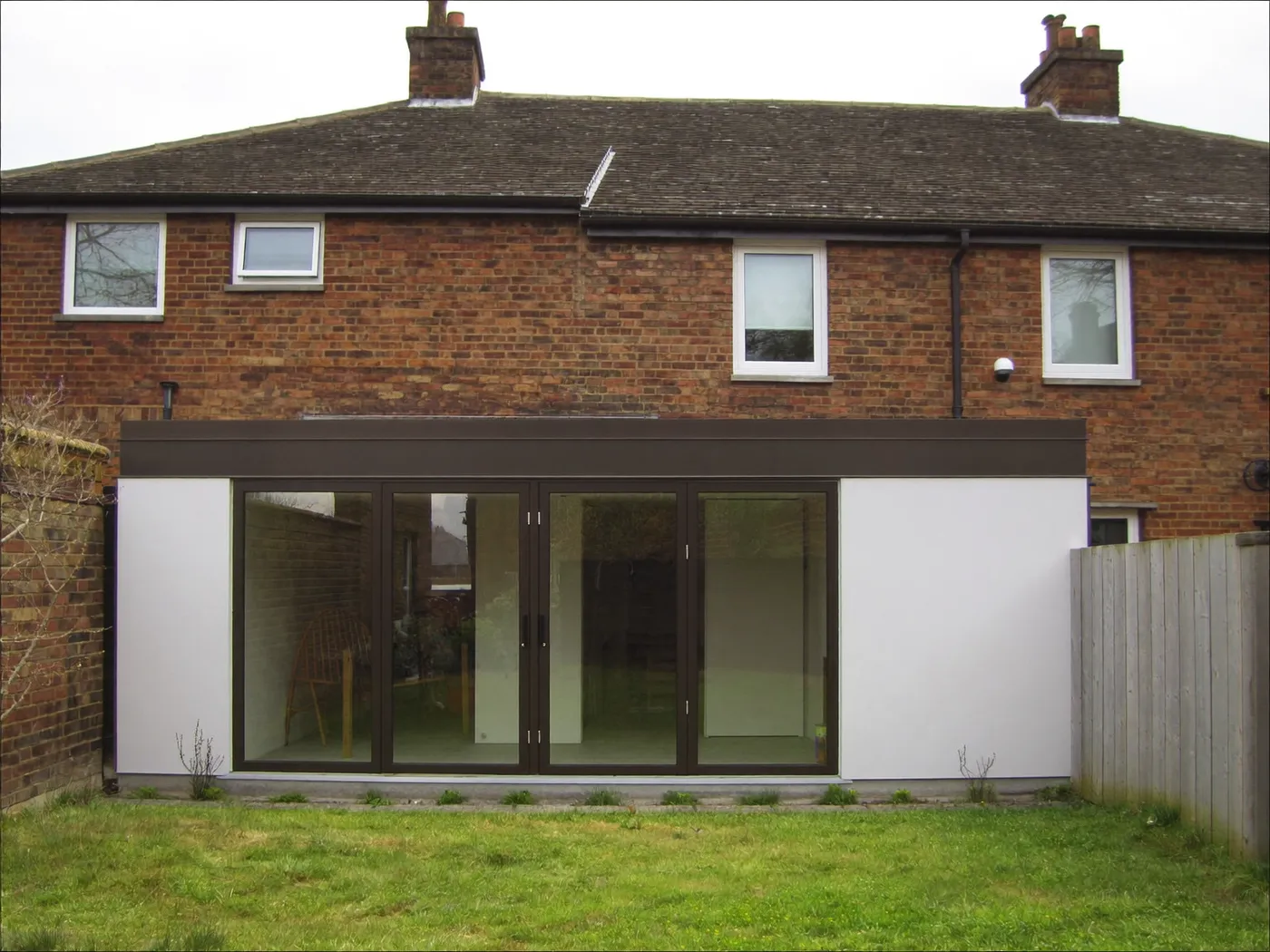 Enfield: single-storey brick rear extension with dark sliding doors onto a lawn