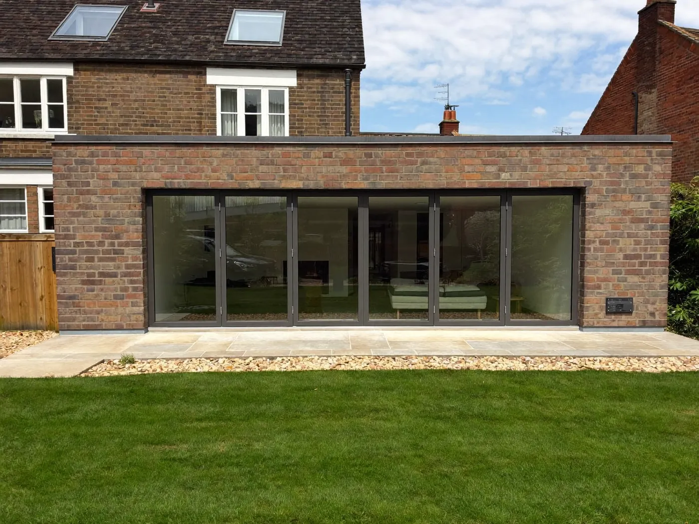 Long single-storey brick rear extension with a flat roof and dark folding glass doors facing a lawn