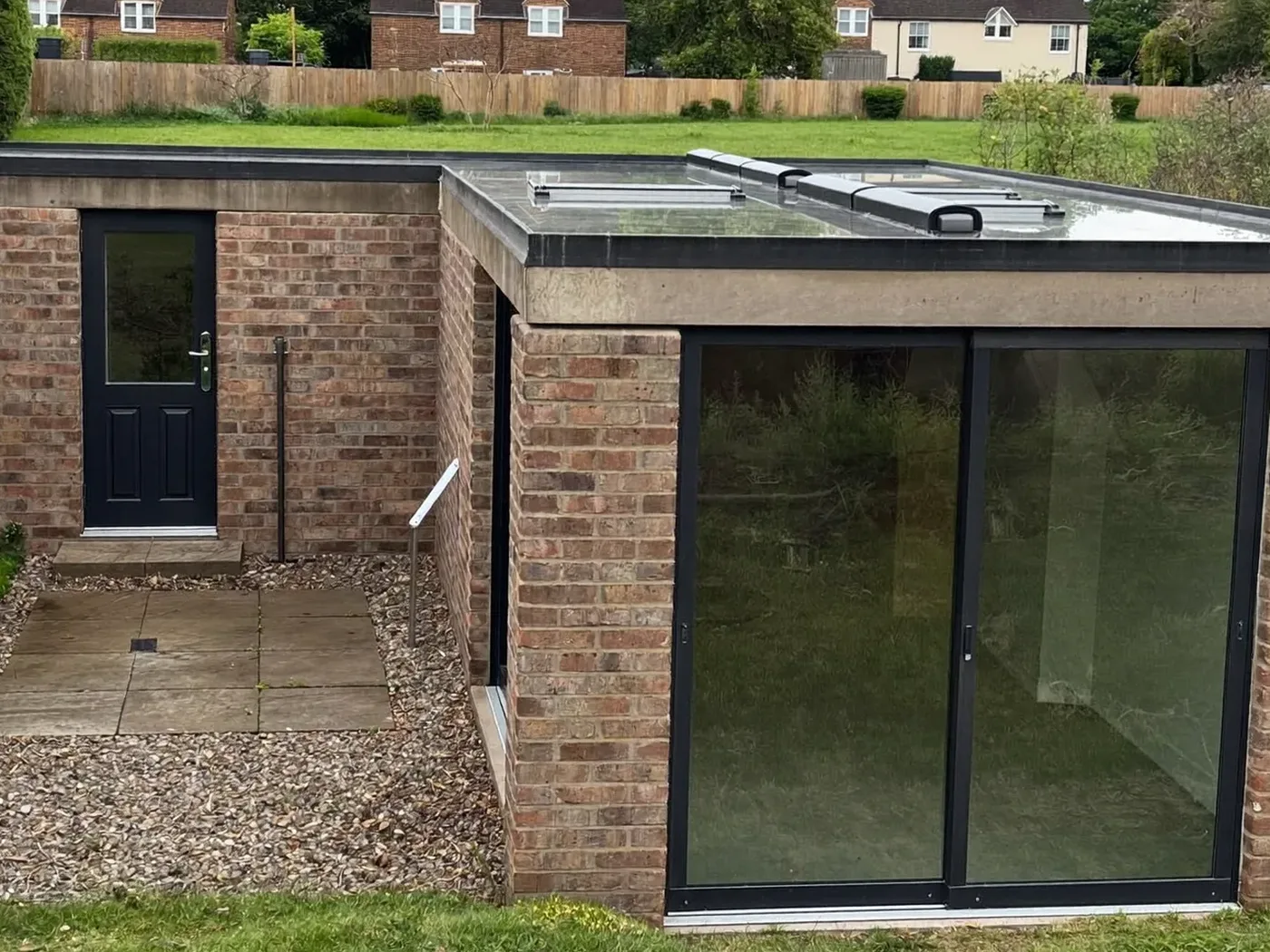 Epsom: L-shaped brick extension wrapping around the back and side of a house with dark sliding doors