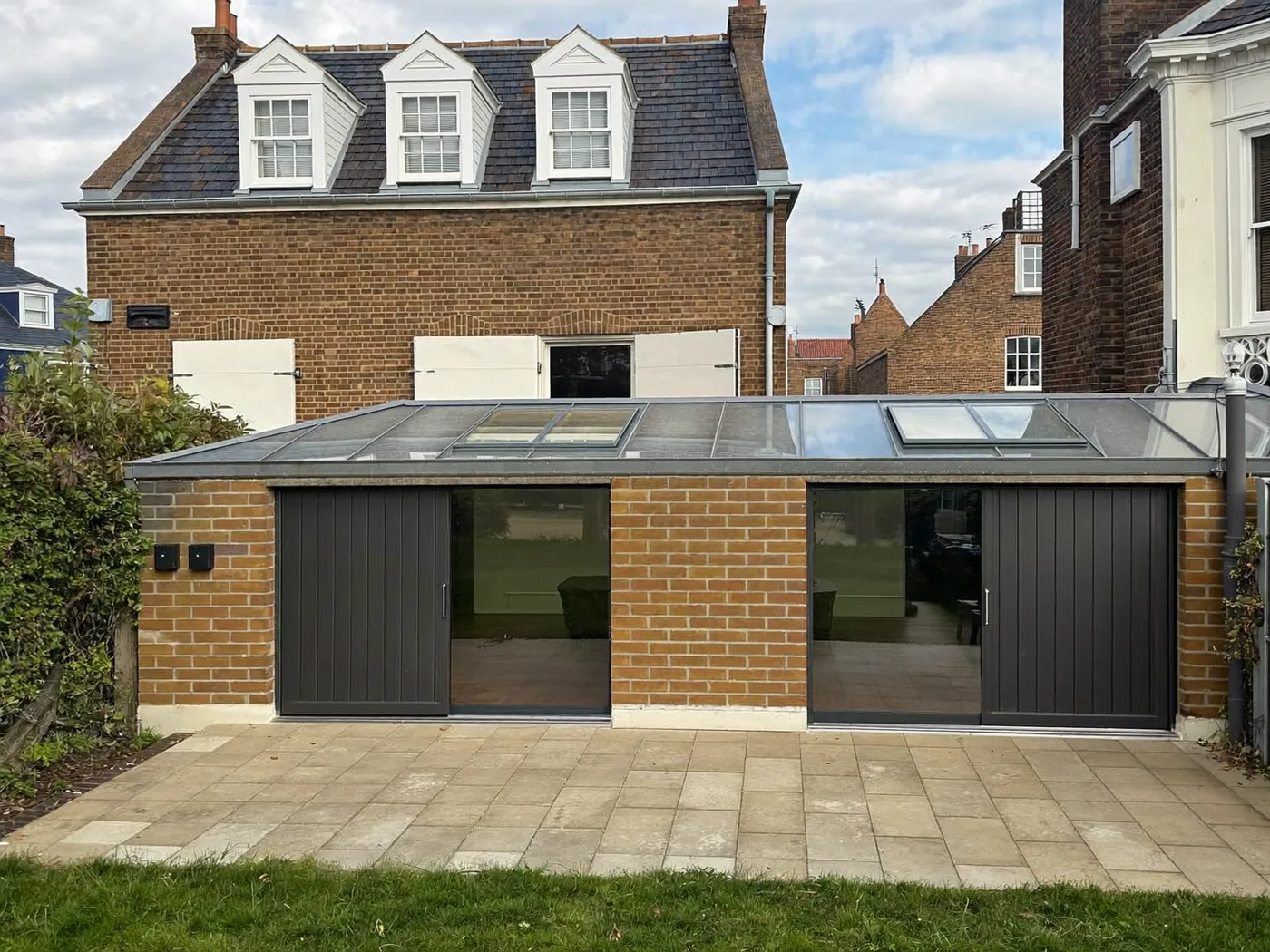 Greenwich: single-storey brick rear extension with dark sliding doors onto a lawn