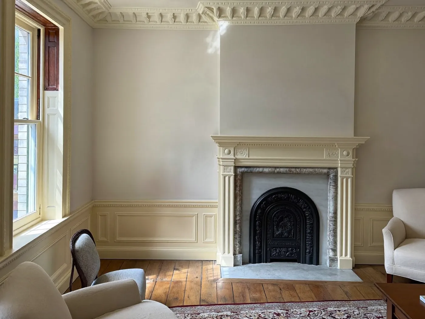 Reception room with a white fireplace, wall panelling, oak floor and a tall sash window