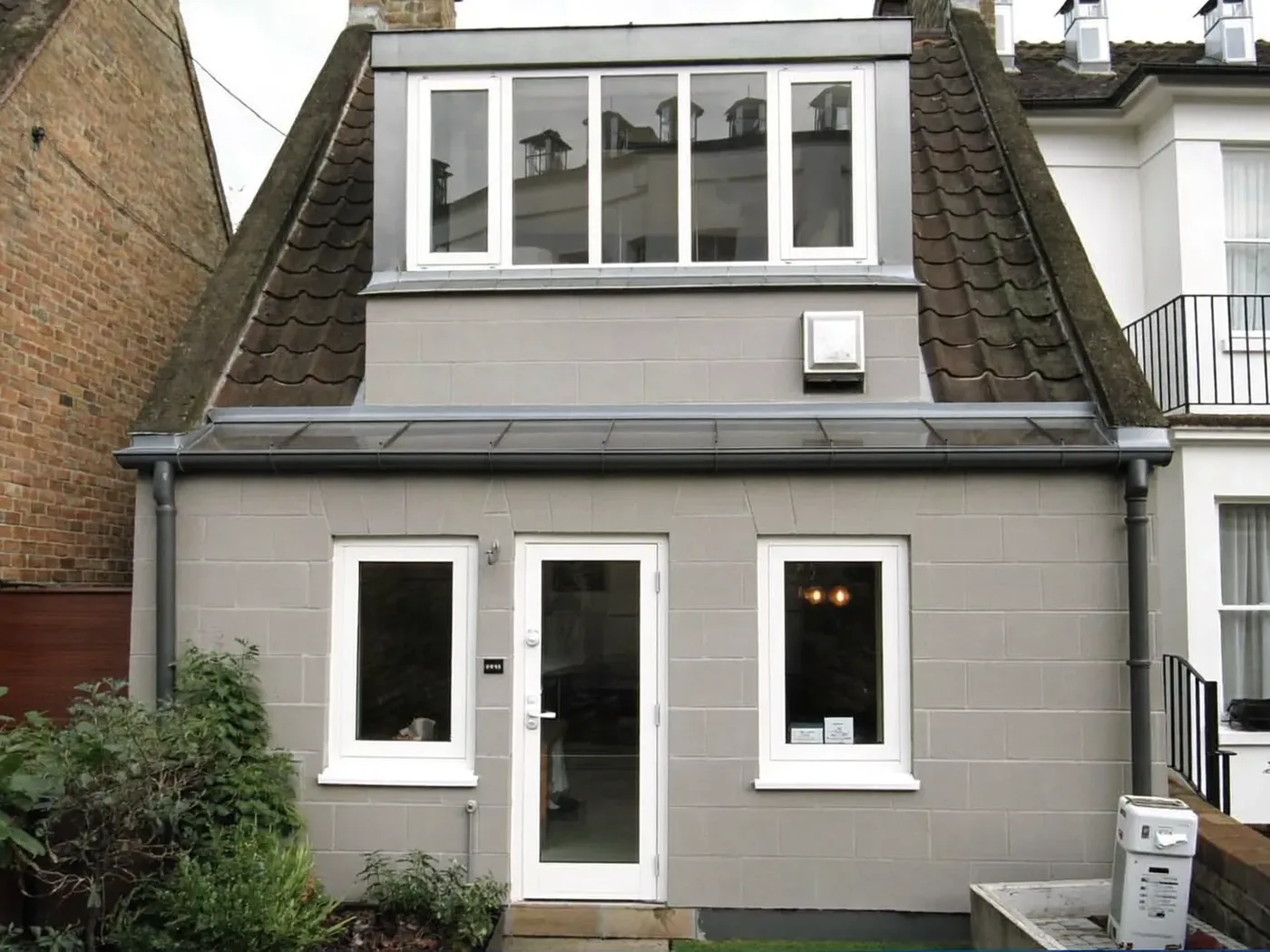 Tile-clad box dormer extension on the rear roof of a rendered house with white-framed windows and a lawn
