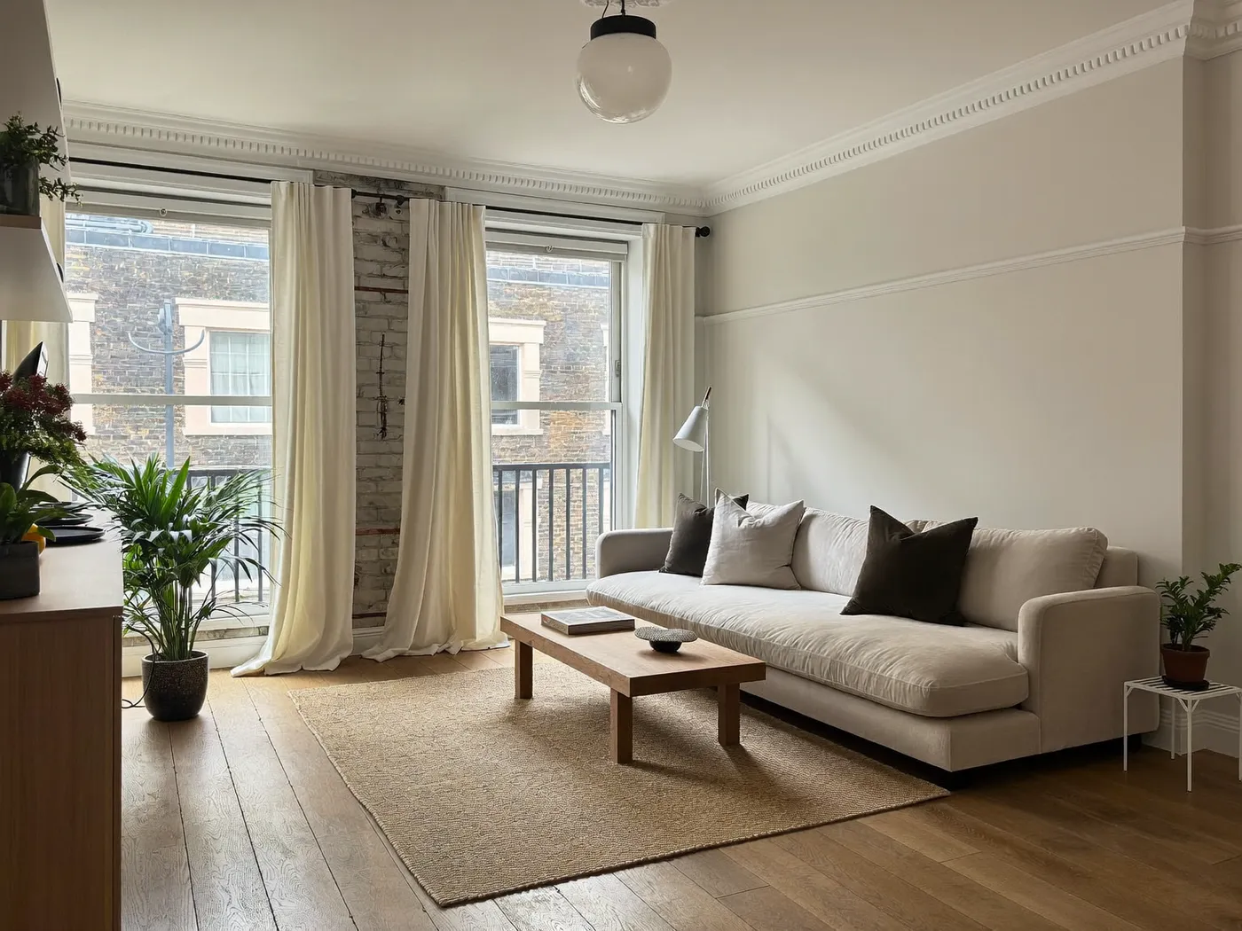 Living room with a beige sofa, wooden coffee table, oak floor and tall windows with long curtains
