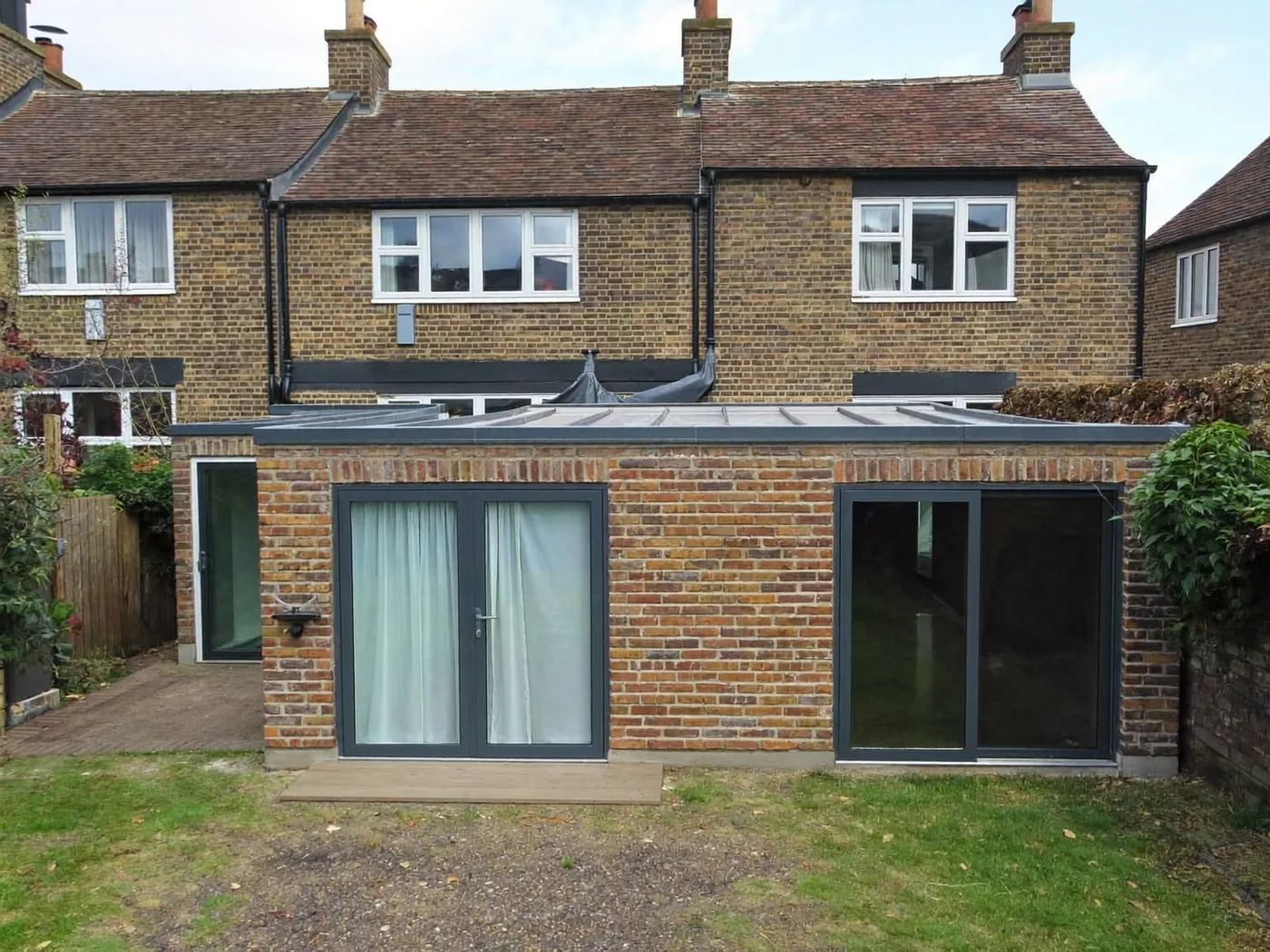 Harrow: L-shaped brick extension wrapping around the back and side of a house with dark sliding doors