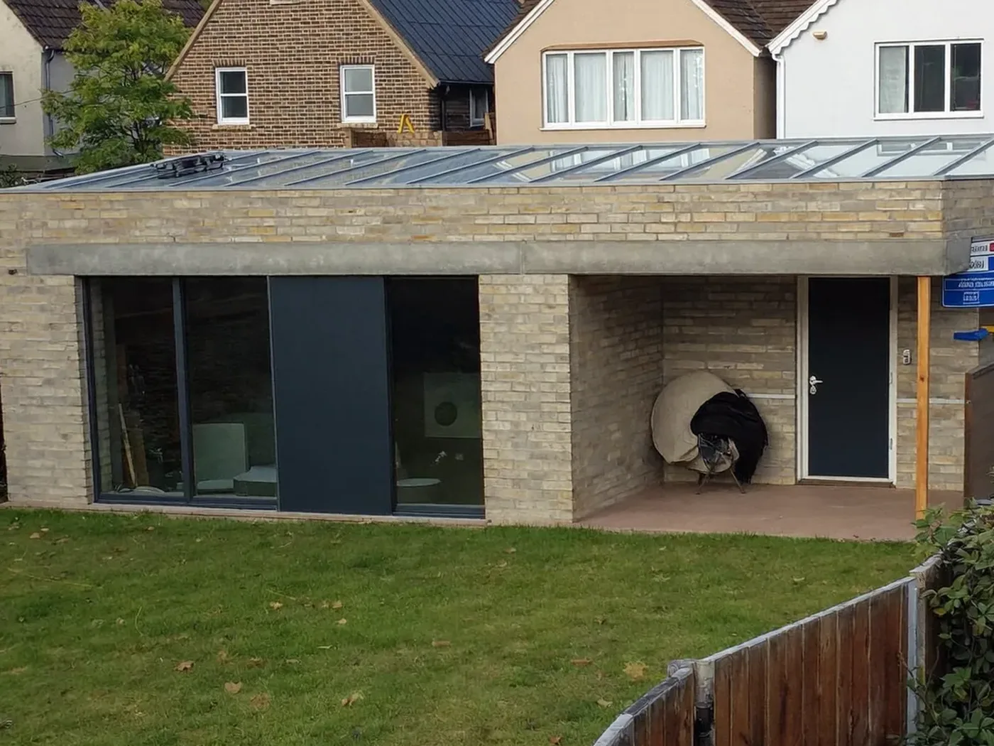 Hertfordshire: L-shaped brick extension wrapping around the back and side of a house with dark sliding doors