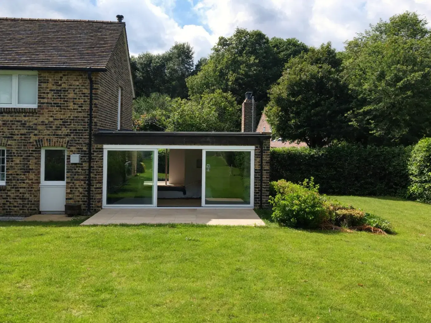 Small flat-roofed rear extension with sliding glass doors on a dark brick house, with a lawn and trees