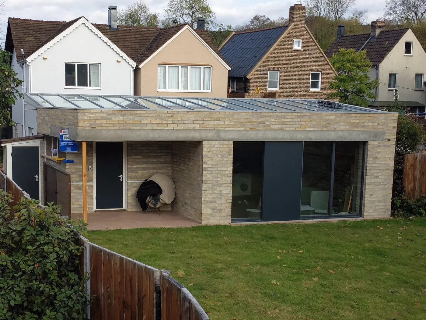 Hillingdon: L-shaped brick extension wrapping around the back and side of a house with dark sliding doors