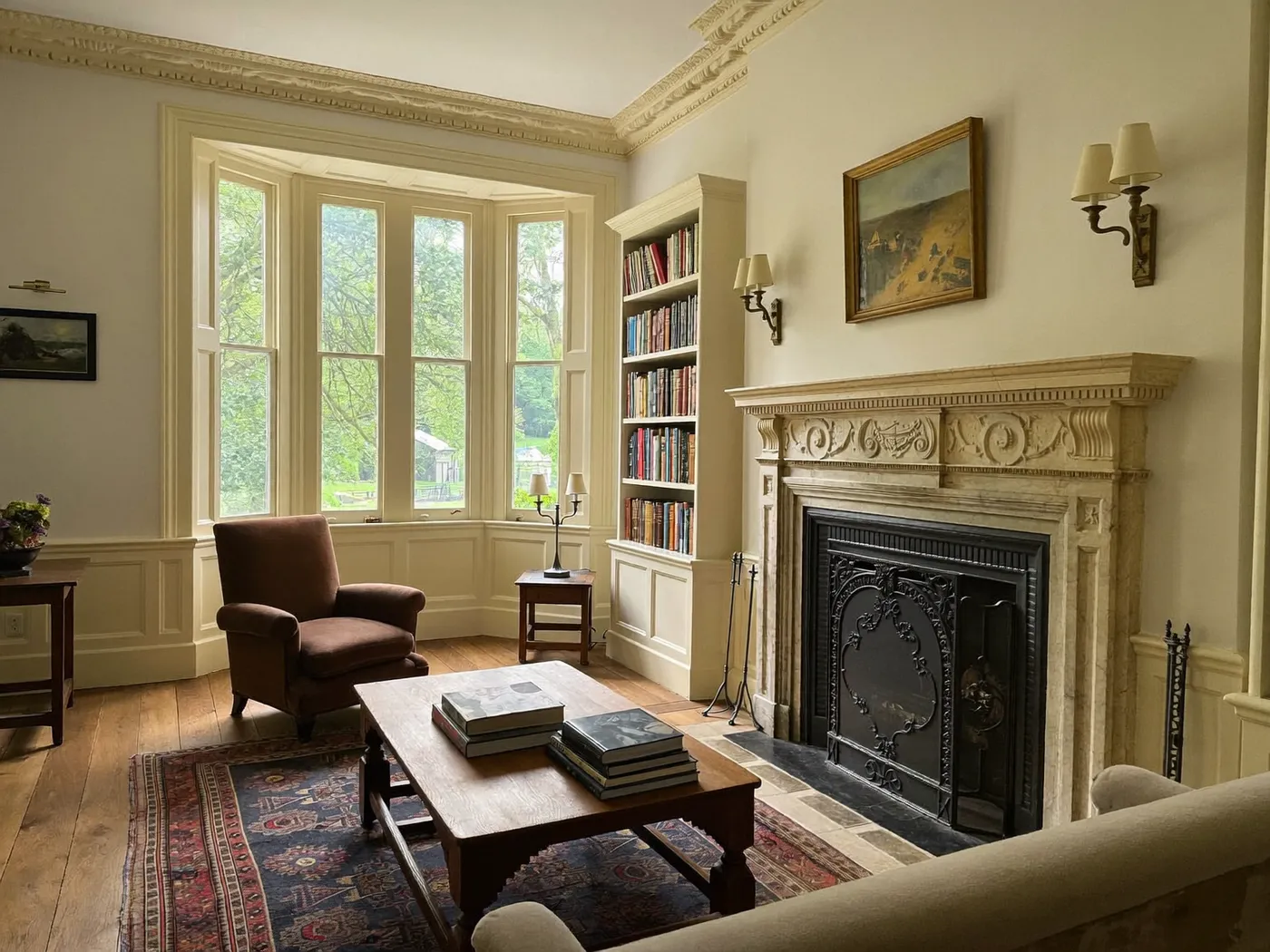 Living room with a cream fireplace, leather armchair, bookshelves, a bay window and a patterned rug