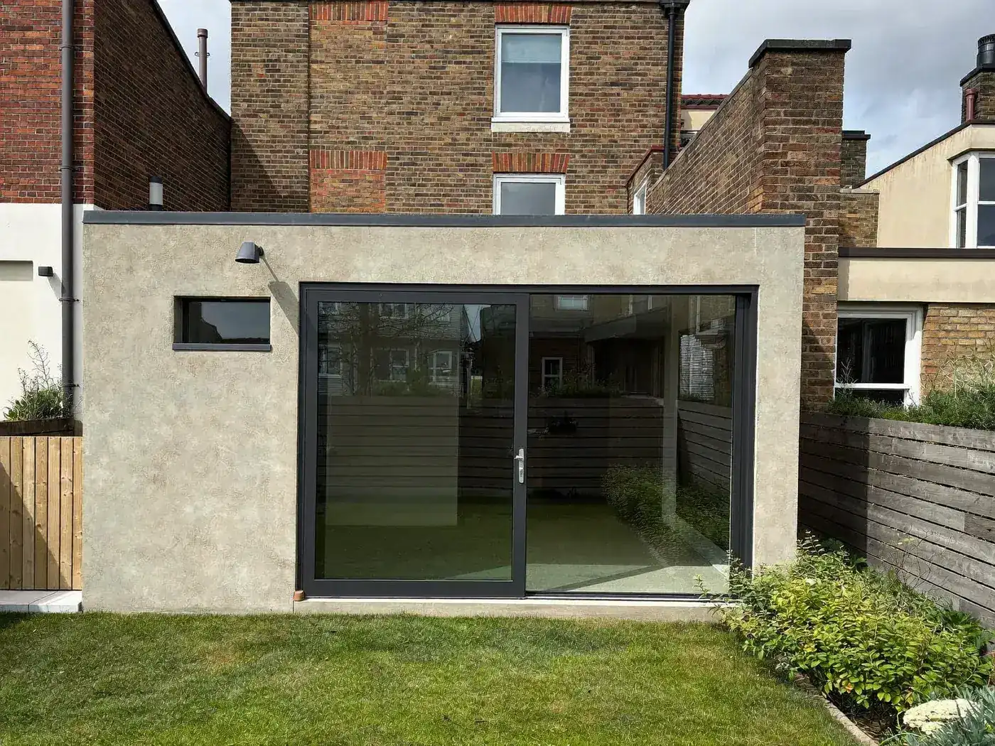 Grey-rendered single-storey rear extension with large dark sliding doors and a flat roof