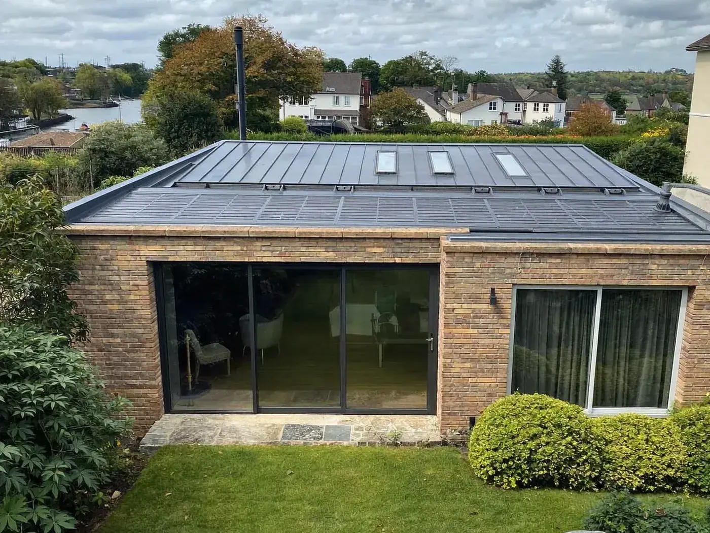 Radlett: L-shaped brick extension wrapping around the back and side of a house with dark sliding doors