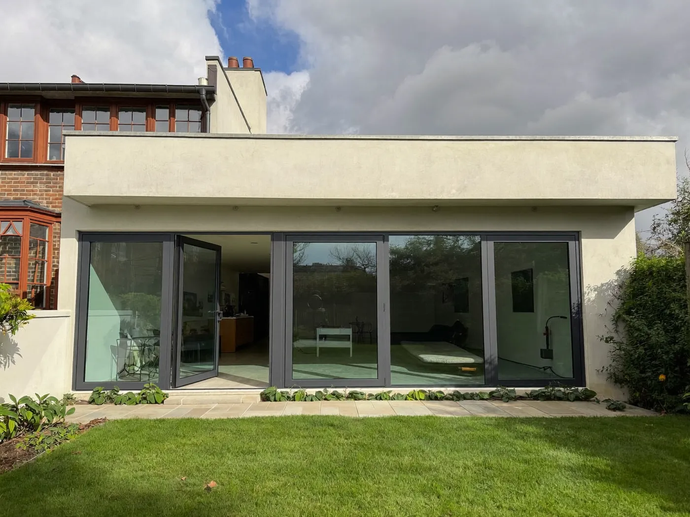 Cream-rendered flat-roofed rear extension with wide folding glass doors on a terraced house