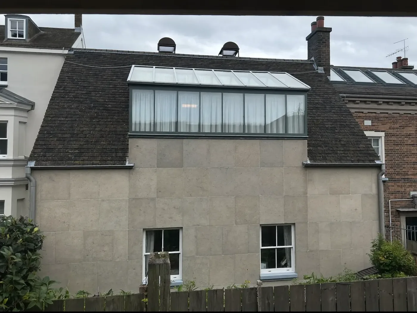 Pitched-roof house with a large grey-clad rear roof extension and roof windows above a lawn