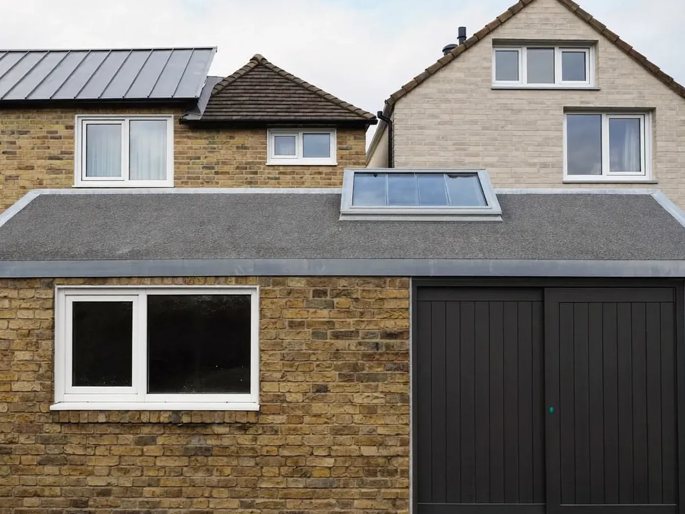 Redbridge: L-shaped brick extension wrapping around the back and side of a house with dark sliding doors