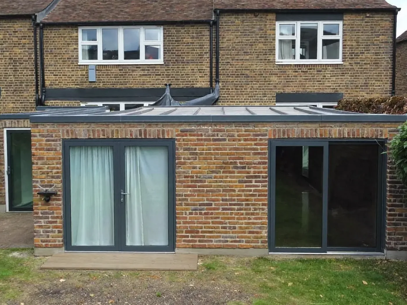 Slough: L-shaped brick extension wrapping around the back and side of a house with dark sliding doors