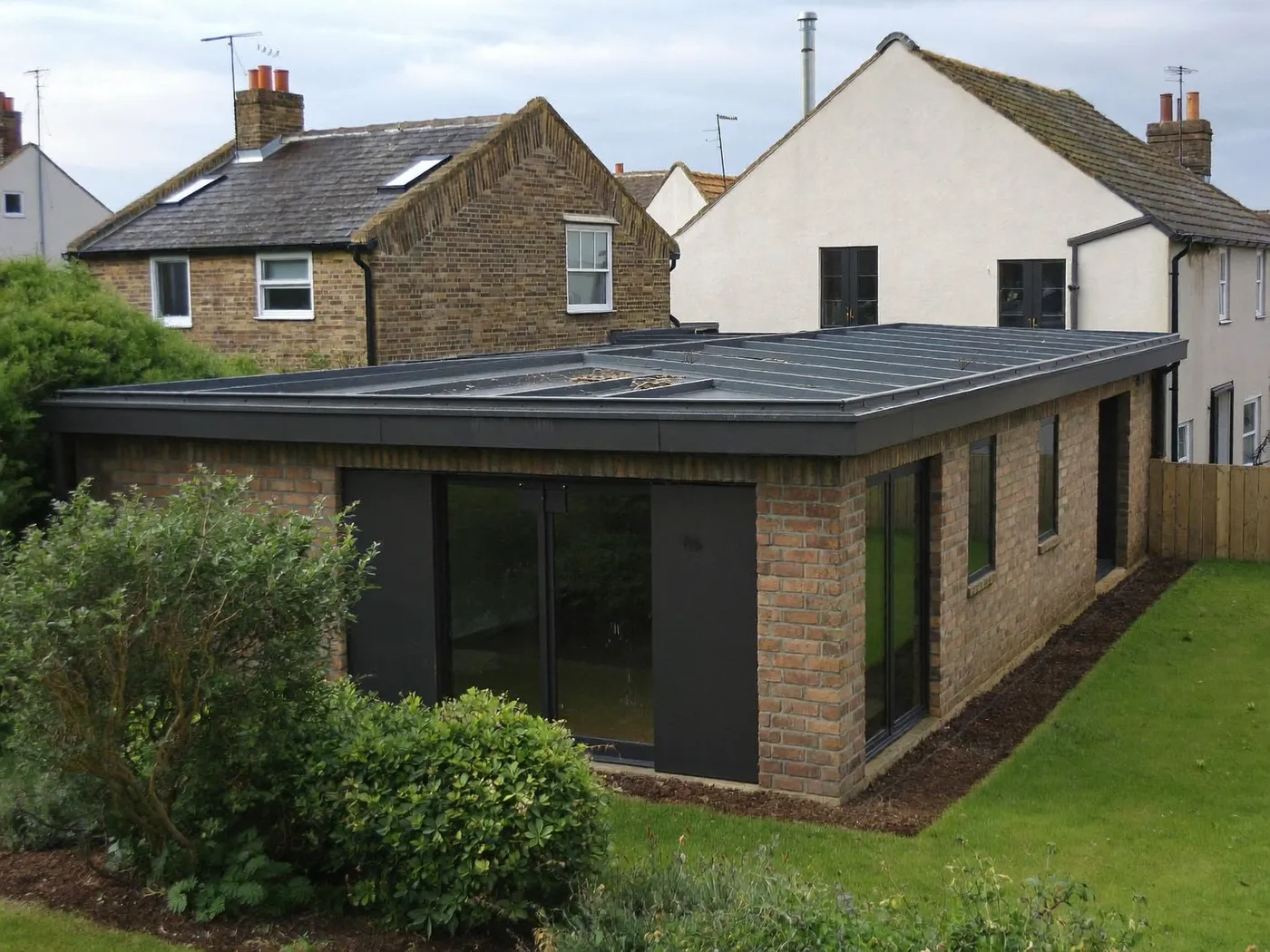 Sutton: L-shaped brick extension wrapping around the back and side of a house with dark sliding doors