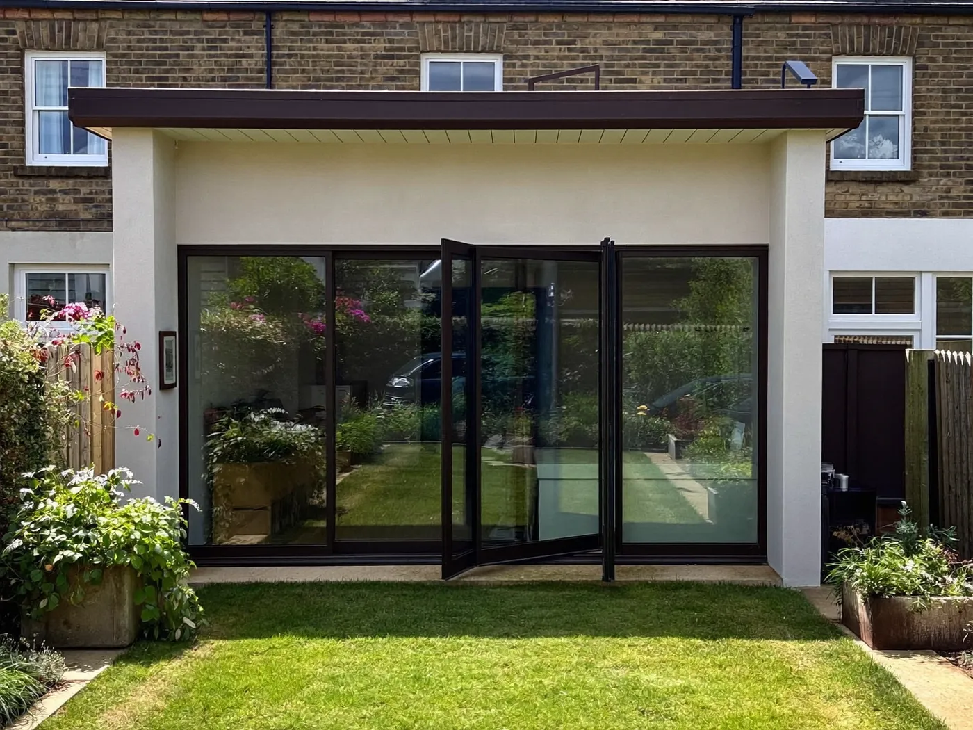 Waltham Forest: single-storey brick rear extension with dark sliding doors onto a lawn