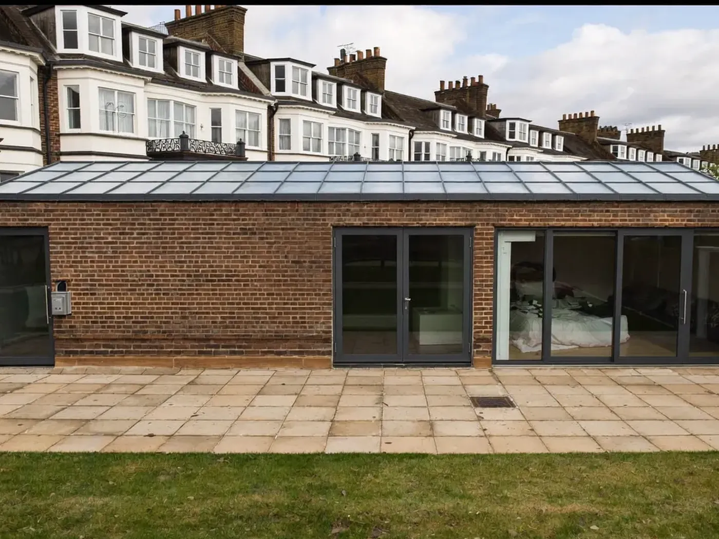 Wandsworth: single-storey brick rear extension with dark sliding doors onto a lawn