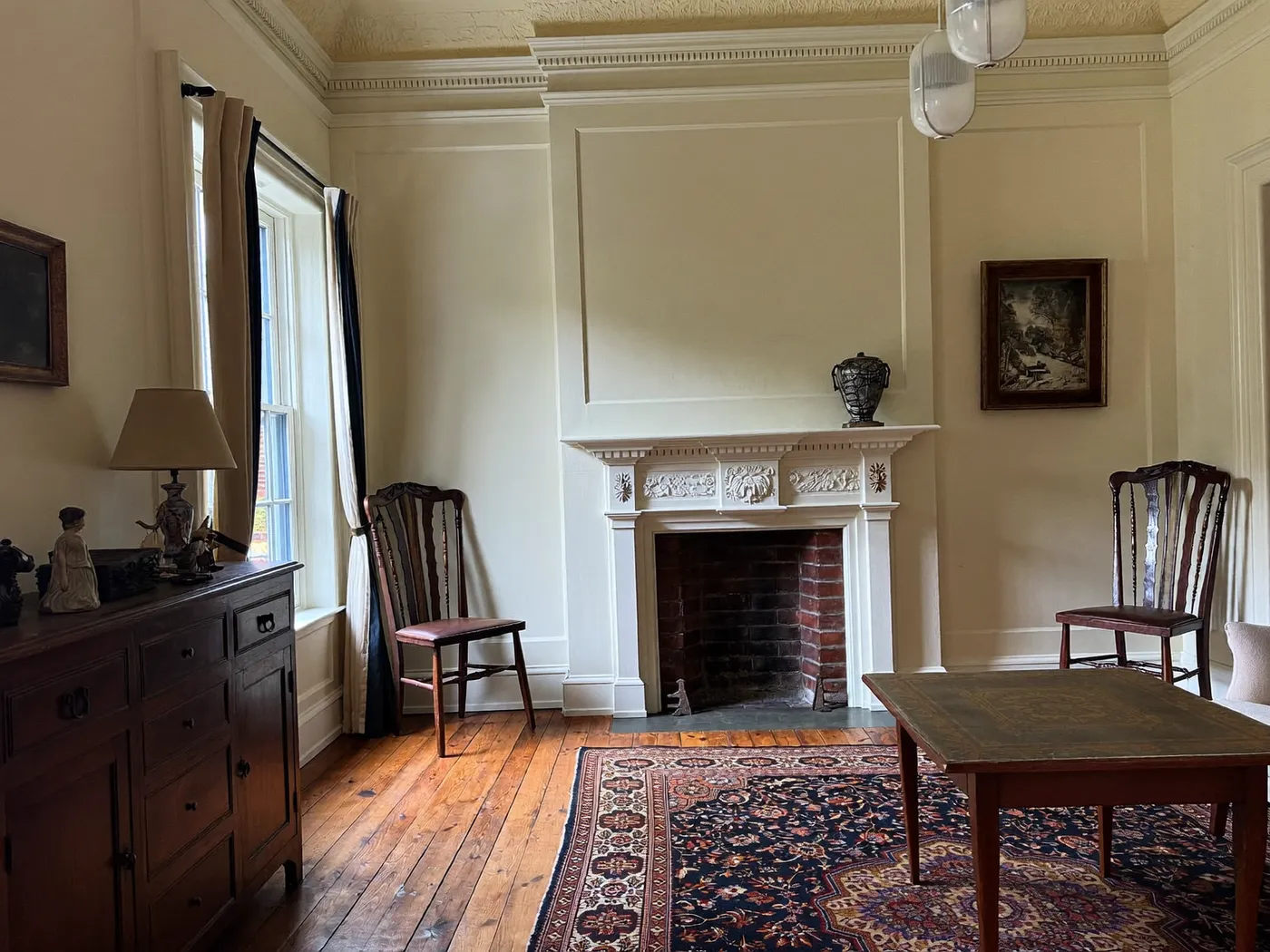 Period reception room with a white fireplace, wooden chairs, a patterned rug and floorboards