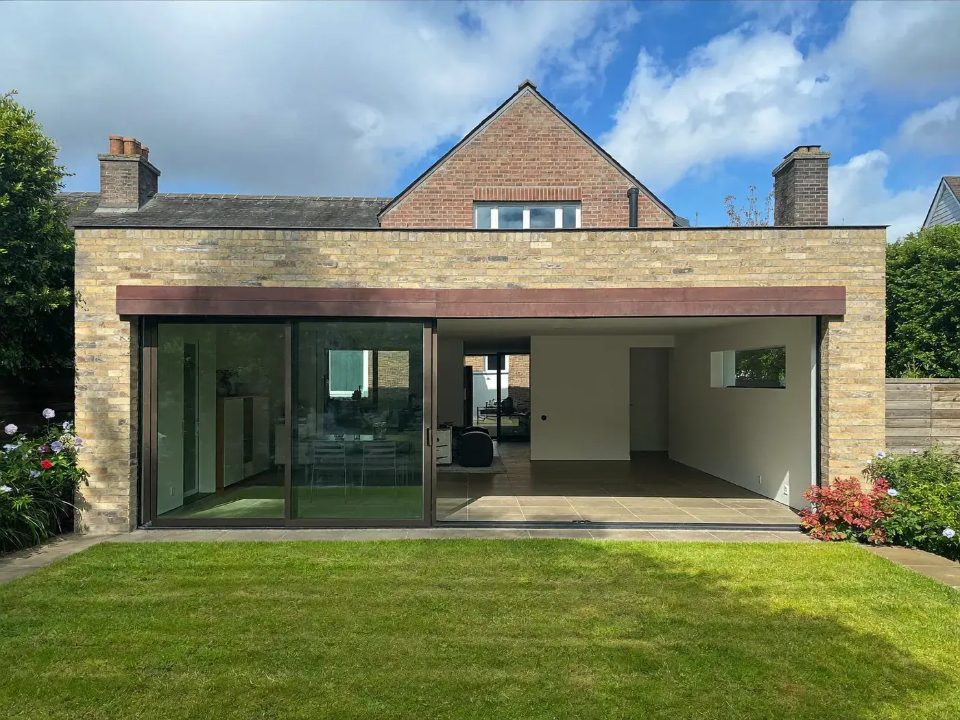 Long brick rear extension with a flat roof and wide sliding doors behind a lawn